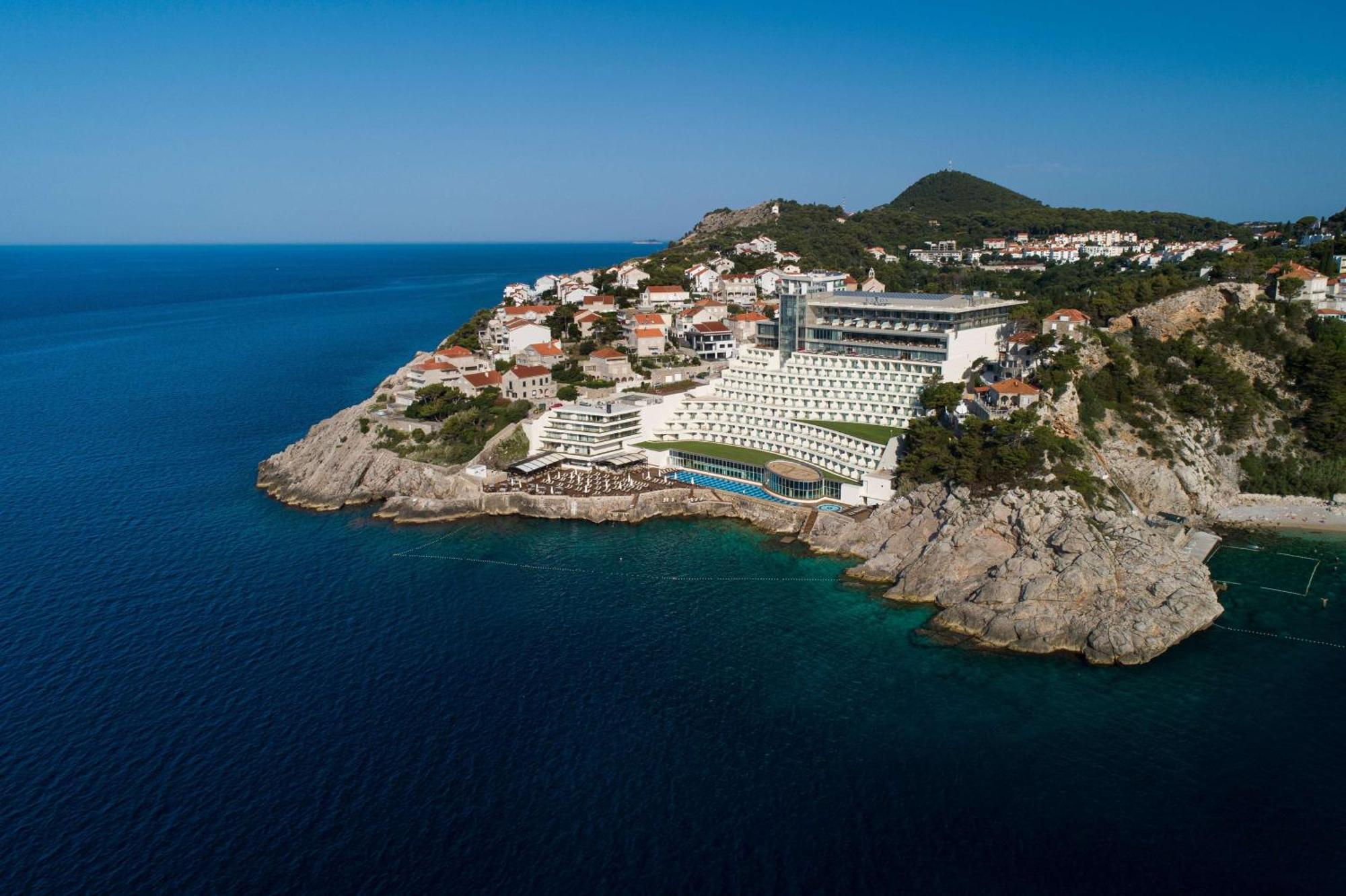 Hotel Rixos Premium Ragusa Esterno foto The photo shows a stunning coastal landscape featuring a modern hotel or resort situated on a rocky outcrop. The building is designed with a contemporary aesthetic, overlooking the deep blue sea. In the background, there are several residential struc